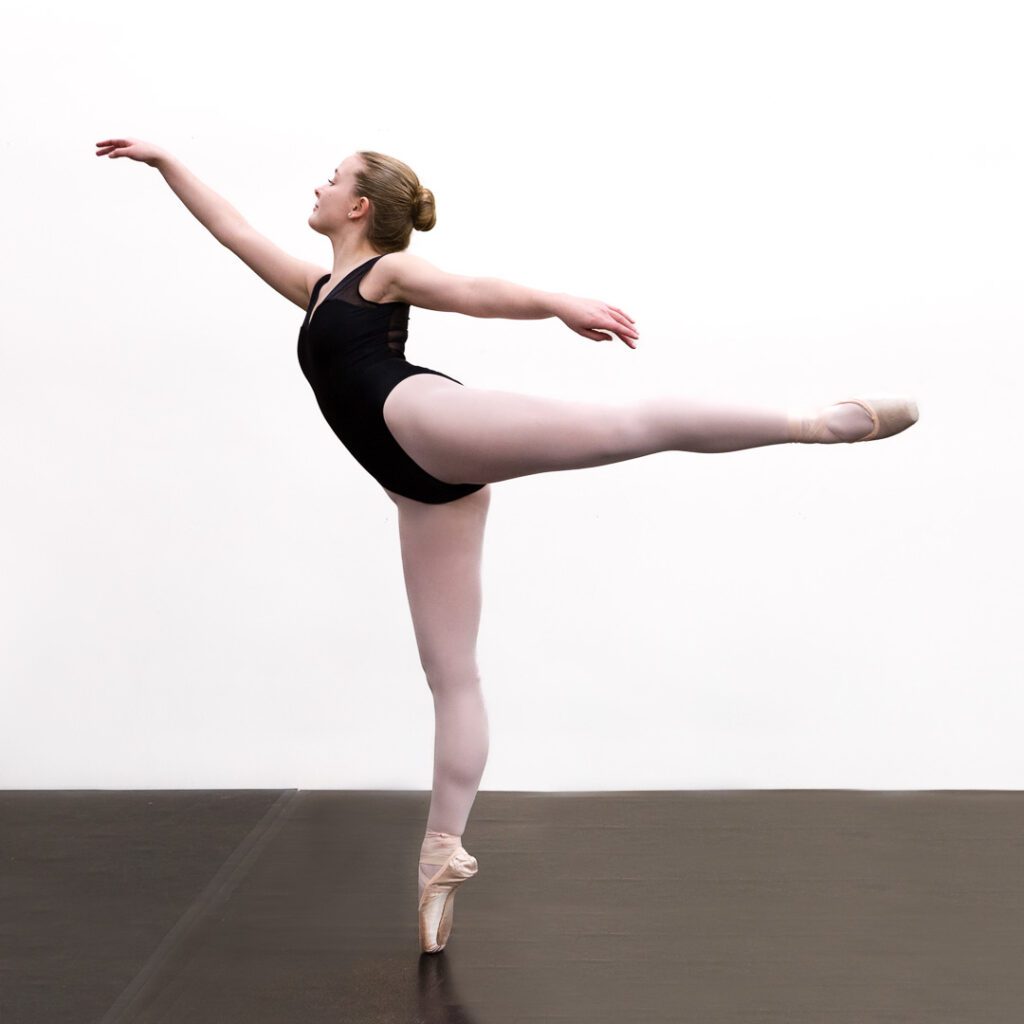 Female ballerina in classic pink tights & black leotard on pointe in arabesque.