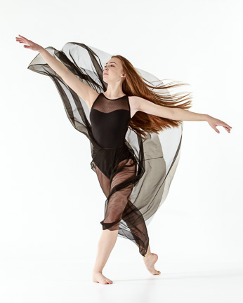 Female dancer, standing with one foot pointed behind, flowing skirt & hair blowing in wind